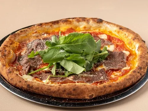 Domates Soslu Biftekli — Dana bonfile, parmesan, domates sosu, mozzarella, taze fesleğen, çeri domates, roka, trüf yağı ve zeytinyağı.